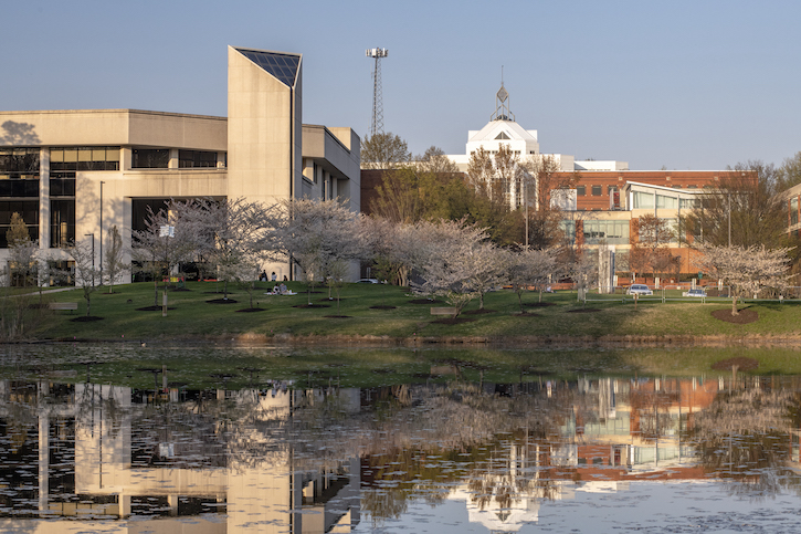 A view of George Mason University's campus in Fairfax, Virginia. A pond is in the foreground, and campus buildings appear in the back. 