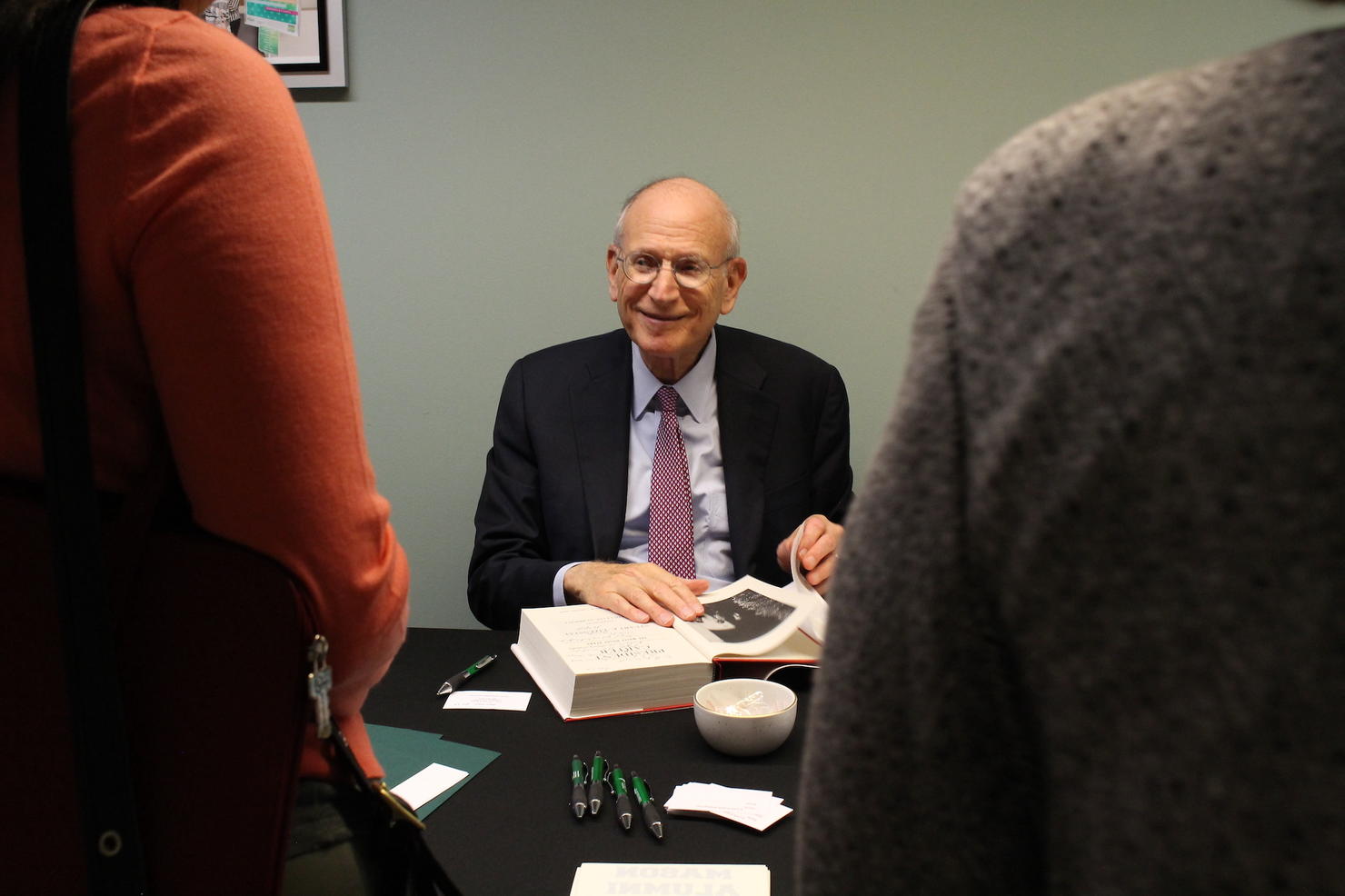 Stuart Eizenstat sitting at a table and signing copies of his book.