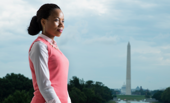 A young Black woman smiles with the Washington monument and reflecting pool in the background.