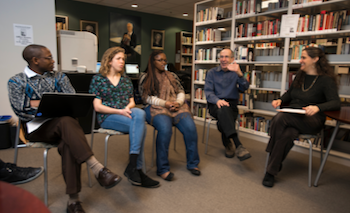 Five people chat and laugh while seated in a library.