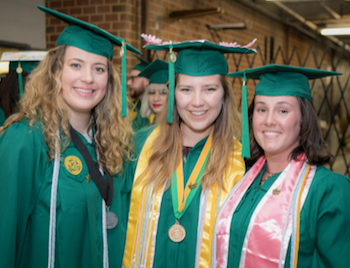 Three young woman in green graduation robes and mortar boards smile at the camera.