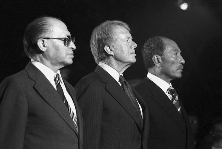 A striking black and white photo of Menachem Begin, Jimmy Carter, and Anwar Sadat in profile, each staring in the same direction.