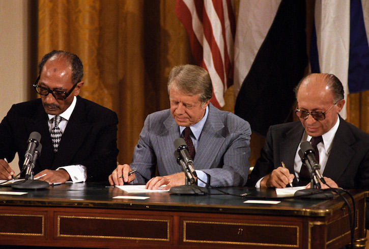 Color photo of Anwar Sadat, Jimmy Carter, and Menachem Begin at an official table signing the 1978 Camp David accords.