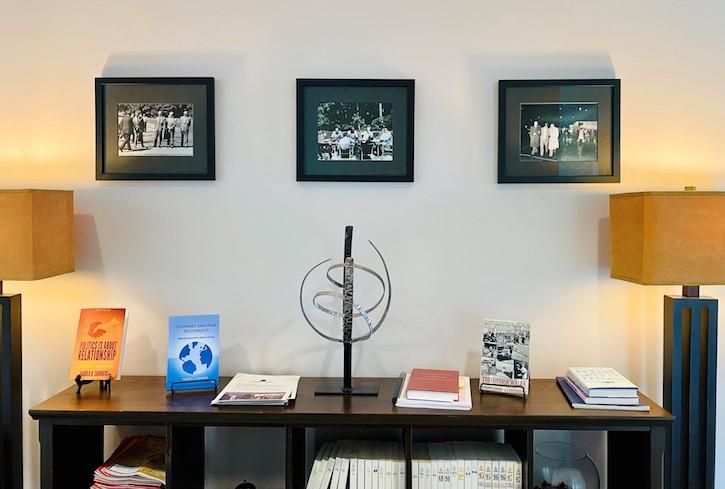Photo of three framed photos on a wall above a wooden bookshelf with Hal Saunders's books on the top.