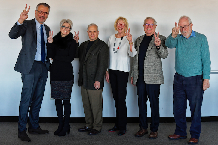 Alpaslan Ozerdem, Sara Cobb, Kevin Avruch, Sandra Cheldelin, Rich Rubenstein, and Chris Mitchell hold up peace signs while standing in Room 5183 at the Carter School on the Arlington Campus.