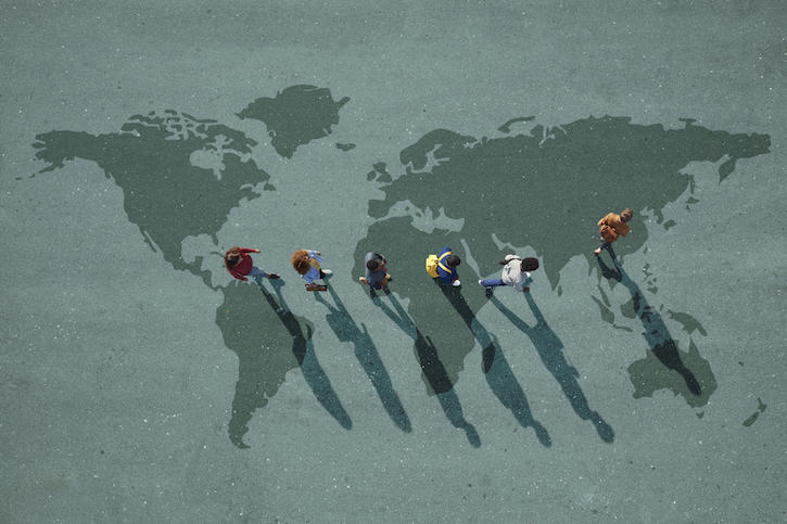 Photo of a line of young people in backpacks walking across a world map painted on green asphalt.