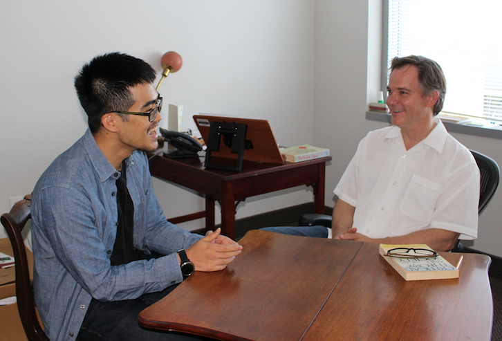Ryan Chiu, a master's student, and Solon Simmons, a professor, sit at a wood table in Simmons's office and chat. Both are smiling and laughing.