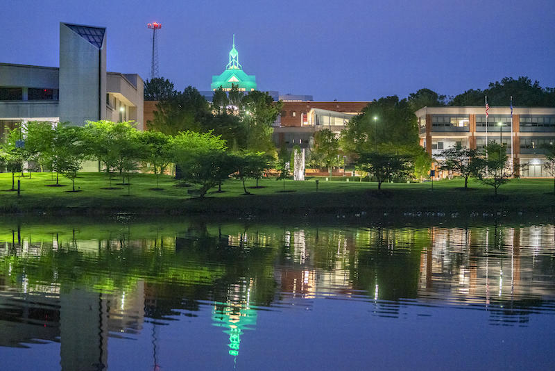 Night time view of Fairfax Campus with buildings illuminated and reflected in pond