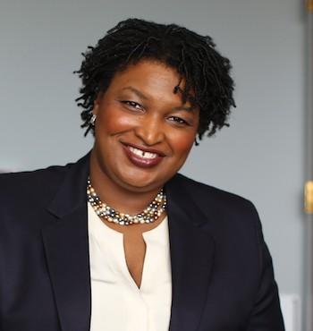 Stacey Abrams portrait. She smiles at the camera wearing a beaded pearl necklace and sport jacket
